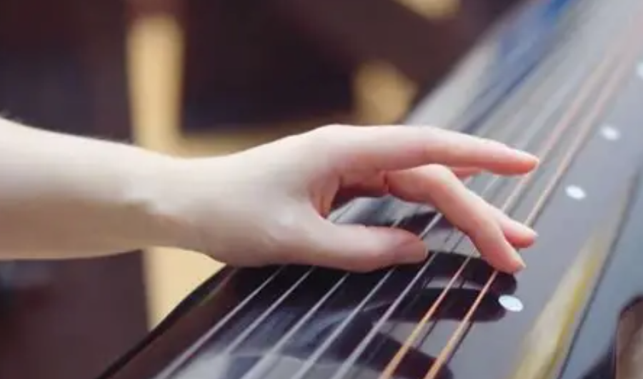 Close-up of the left hand pressing guqin strings beside the hui position markers.