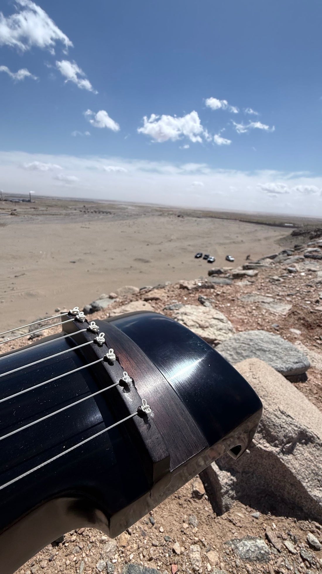 A black guqin resting on desert rocks under a vast open sky — photographed by William Xu at Yinshan Grand Canyon, 2024