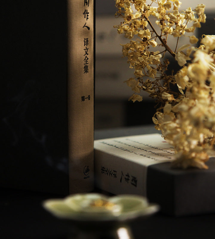 A volume of Zhou Zuoren's collected translations beside pale flowers; an atmospheric portrait of the writer, not the source of the guqin essay