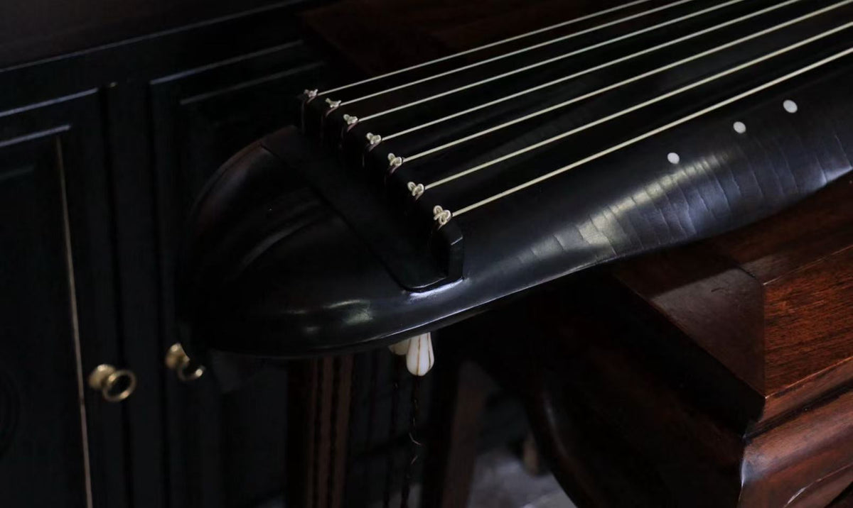 Close-up of seven strings stretching across a dark guqin