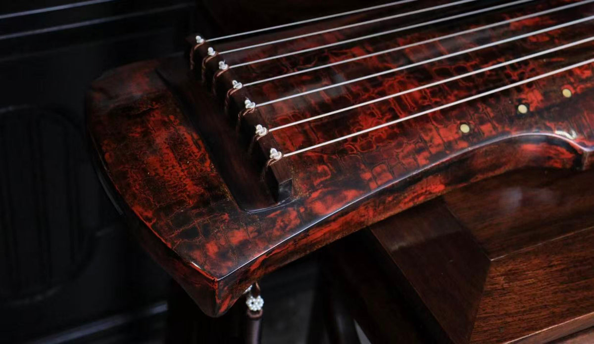 Close-up of seven silk strings on a guqin with red lacquer finish, dramatic lighting