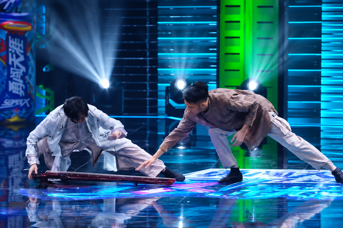 Two dancers on a blue-lit stage in the broadcast work Shou Zhi Yi Qin, one reaching toward a guqin lying on the stage floor