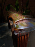 Fuxi style guqin – angled view of upper end showing strings, upper nut and tuning pegs, reflective lacquer surface, garden setting